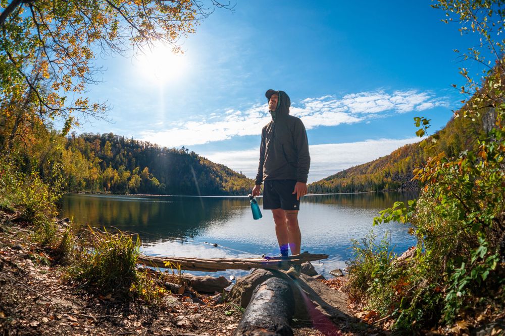 Panoramic view of a serene mountain lake surrounded by colorful fall trees under bright sunlight.