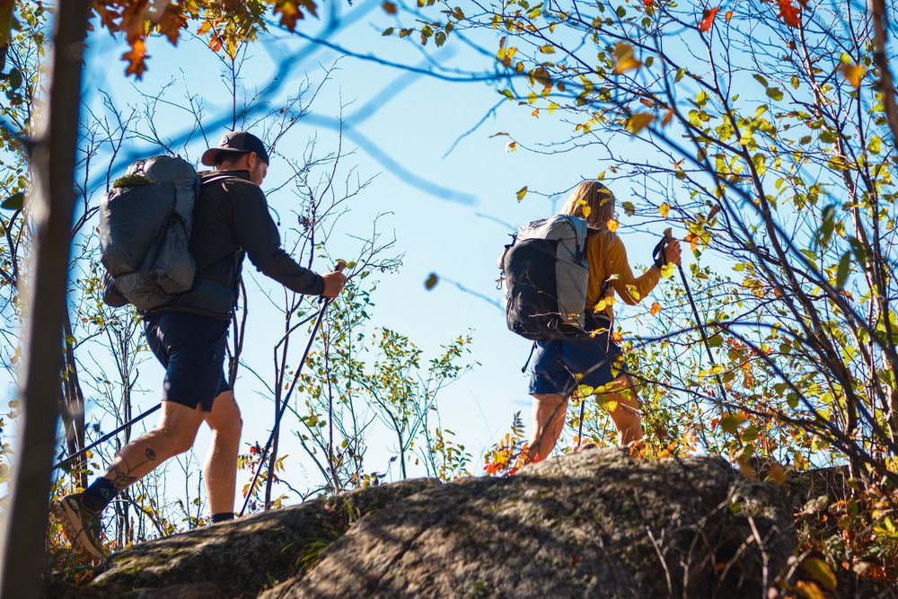 A group of hikers traverse along a narrow mountain ridge trail during autumn with colorful fall foliage.
