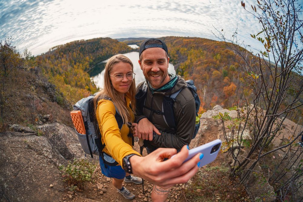A couple enjoys a scenic autumn hike in the mountains with colorful fall foliage in the background.