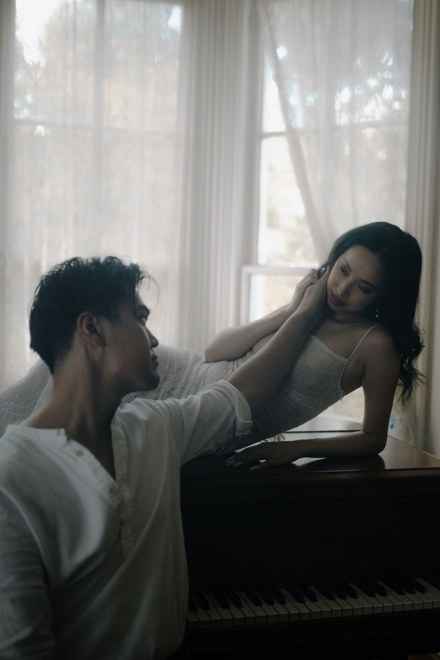 Moody black and white portraits by a piano window showing dramatic poses in soft light.