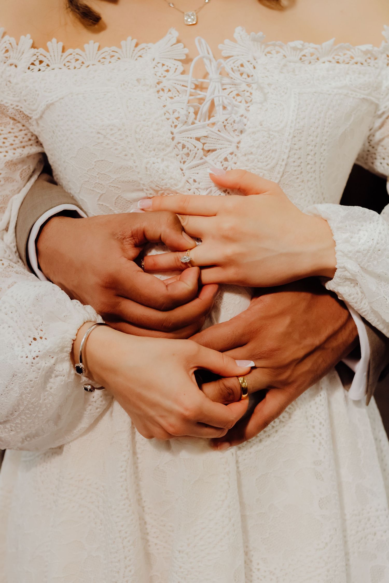 Close up of hands with wedding rings intertwined against white lace fabric.