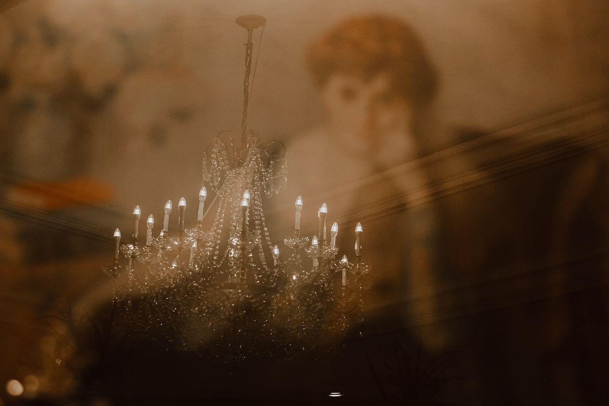 Elegant crystal chandelier with lit candles glowing warmly against a vintage portrait backdrop in sepia tones.