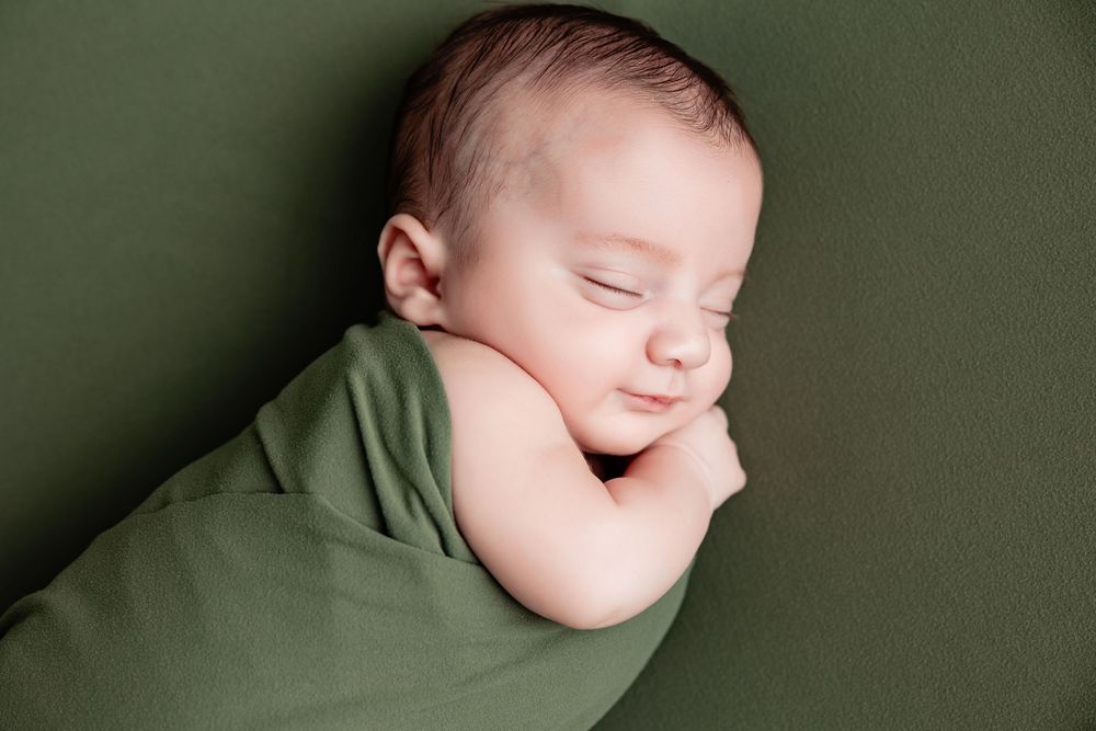 Professional newborn photography portrait of sleeping baby in green swaddle.