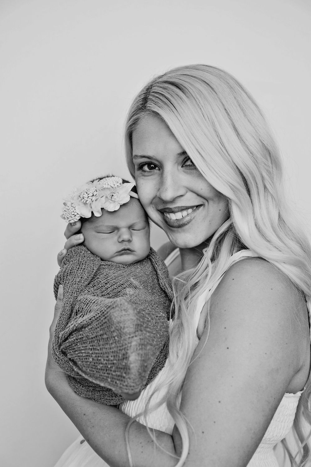 Black and white portrait of a smiling blonde mother holding her sleeping newborn baby.