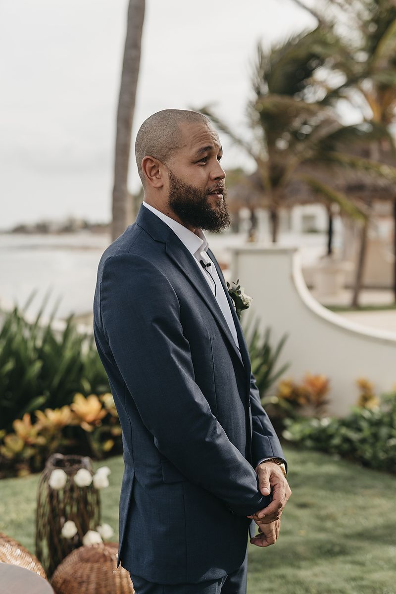Four sequential photos show an emotional groom in a navy suit reacting during a first look wedding moment.