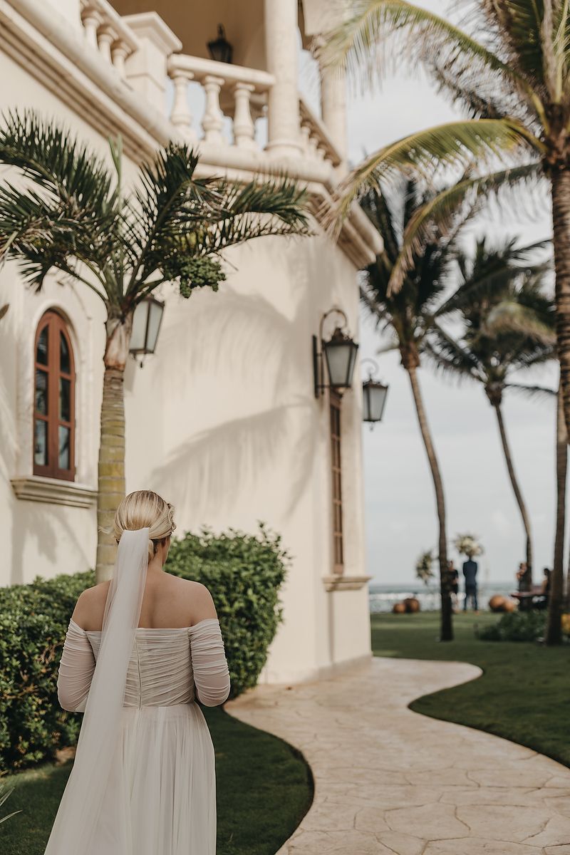 Elegant wedding dress detail at luxurious beachside venue with palm trees and Mediterranean-style architecture.
