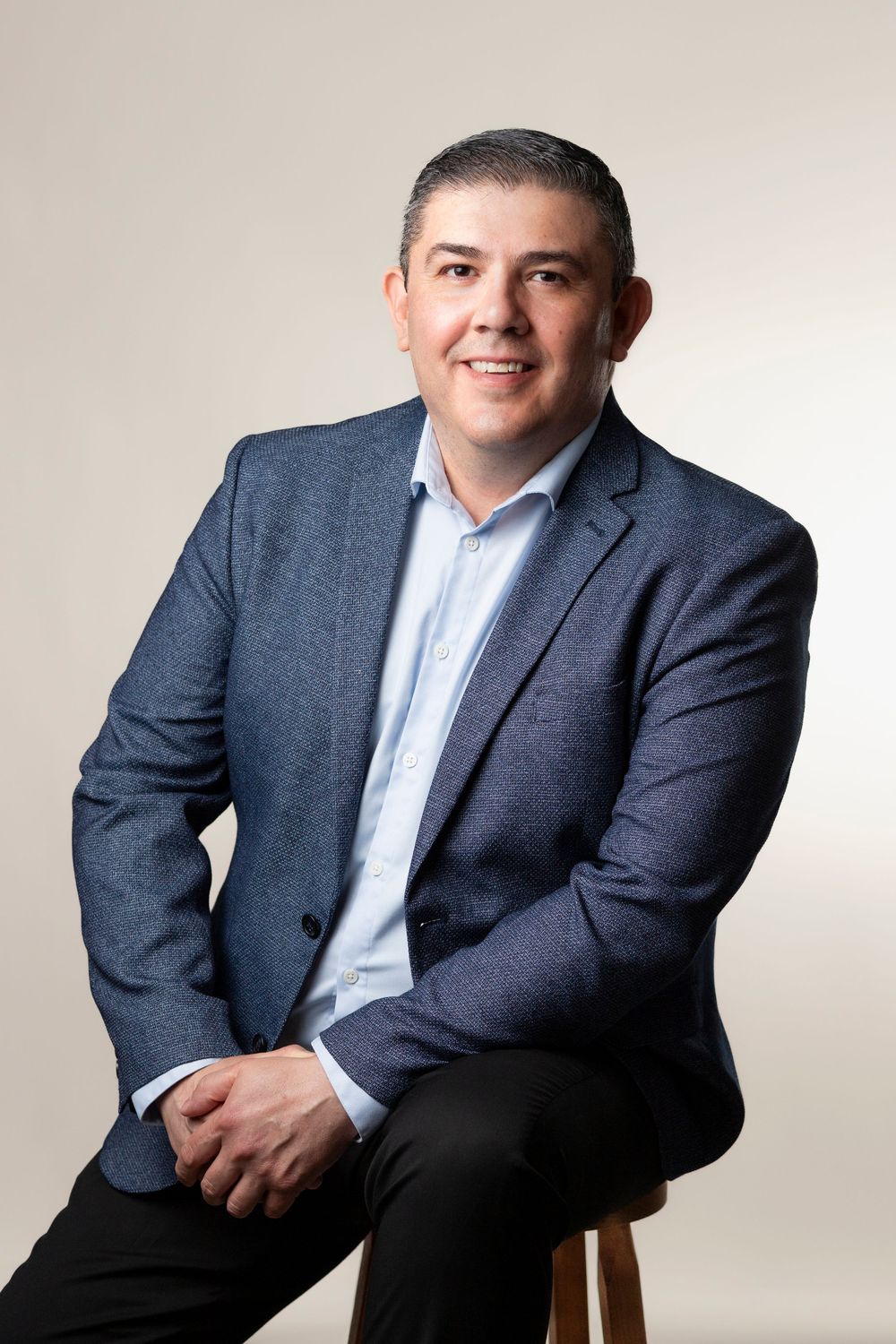 Professional studio portrait of person in navy blazer and light blue shirt against neutral background.