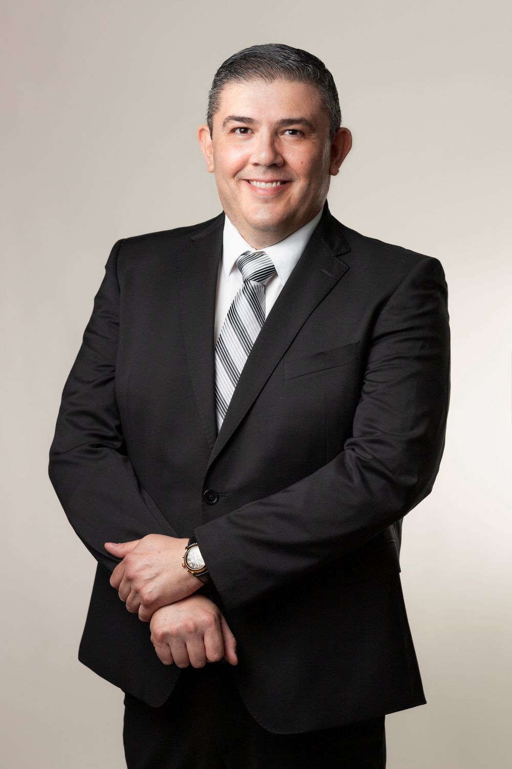 Professional headshot series of person in dark business suit and tie against light backdrop.