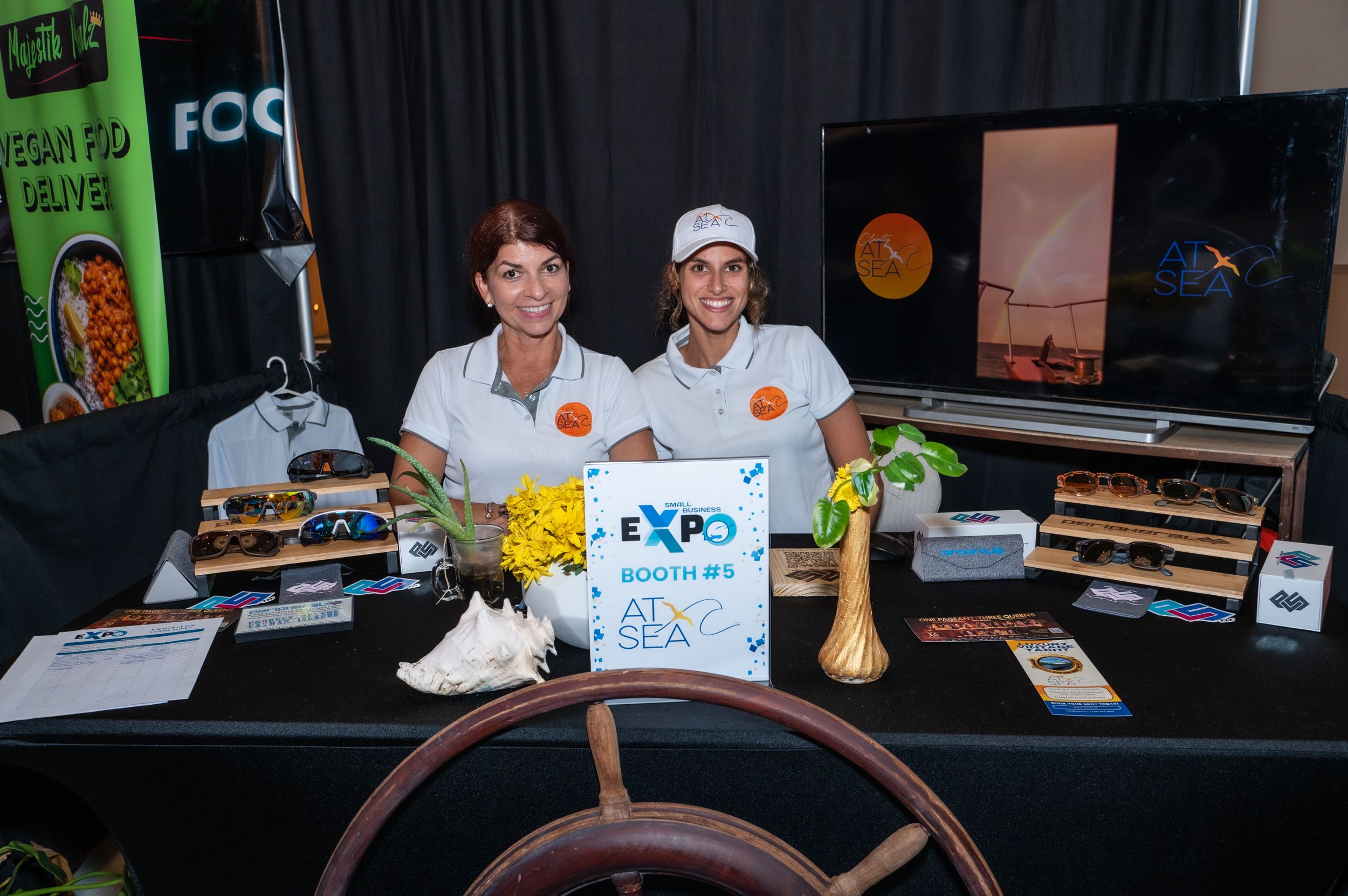 Two women smile at an Expo Booths at Sea trade show booth with nautical decor and displays.