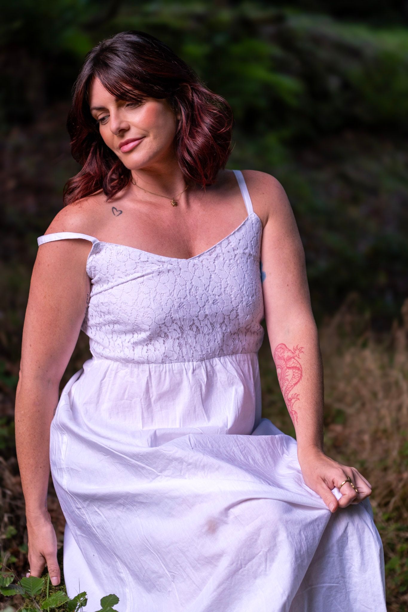 Woman in flowing white summer dress poses gracefully in natural outdoor setting.