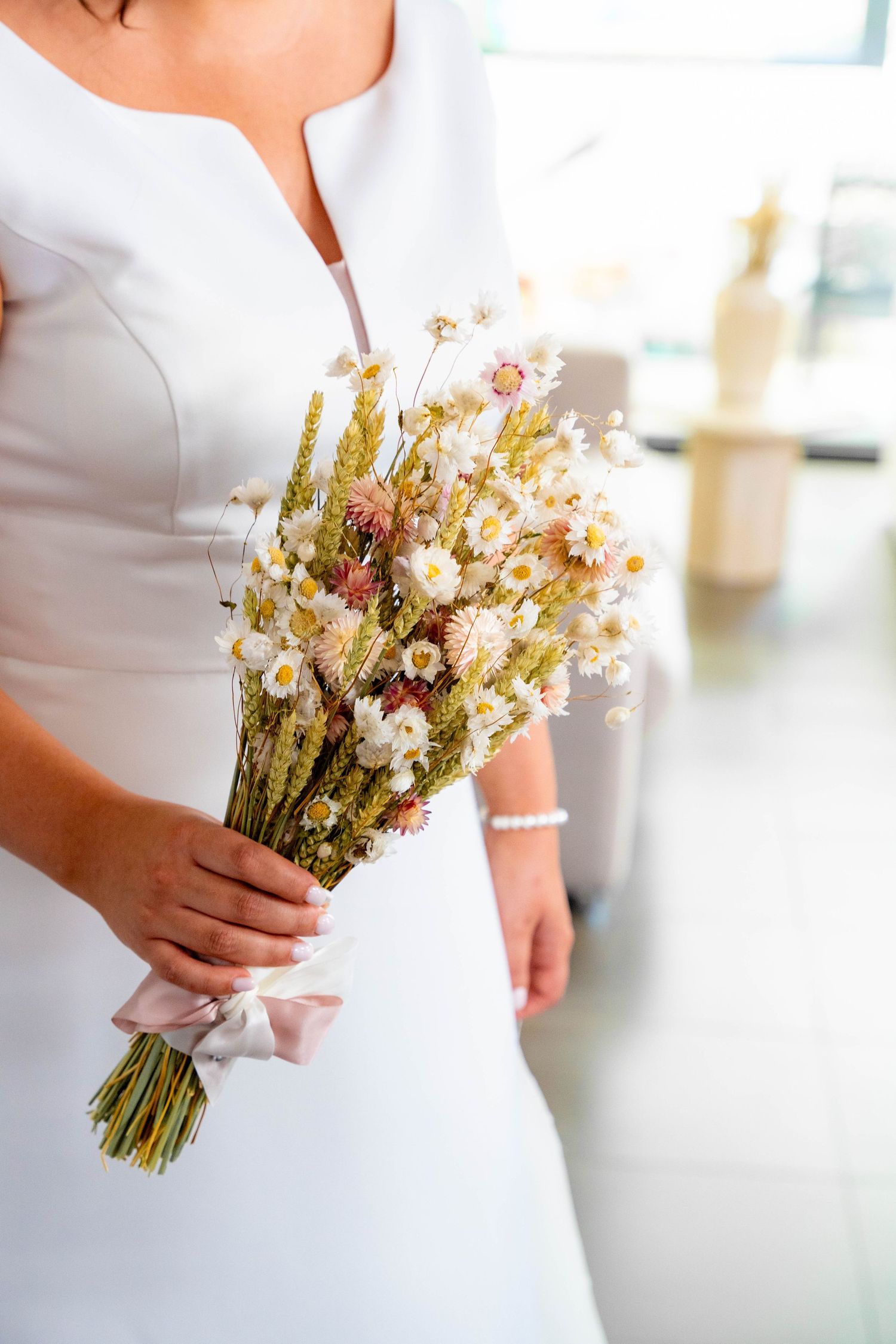 Close-up of a delicate wildflower wedding bouquet held against a white dress.
