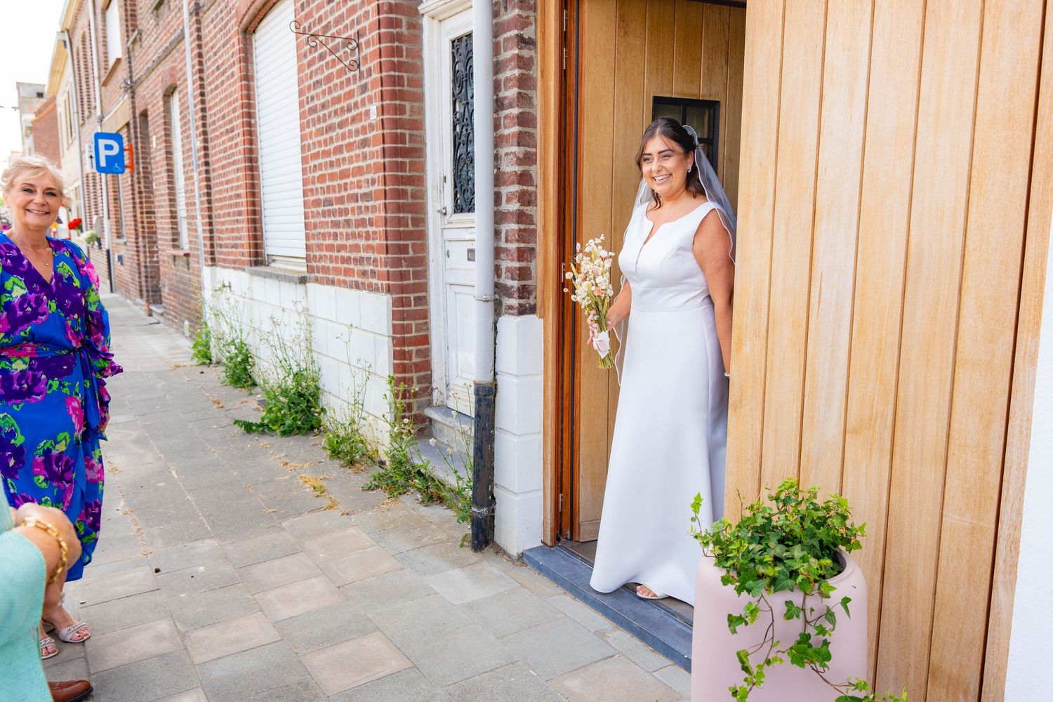 A wedding scene outside a brick building with floral decorations.