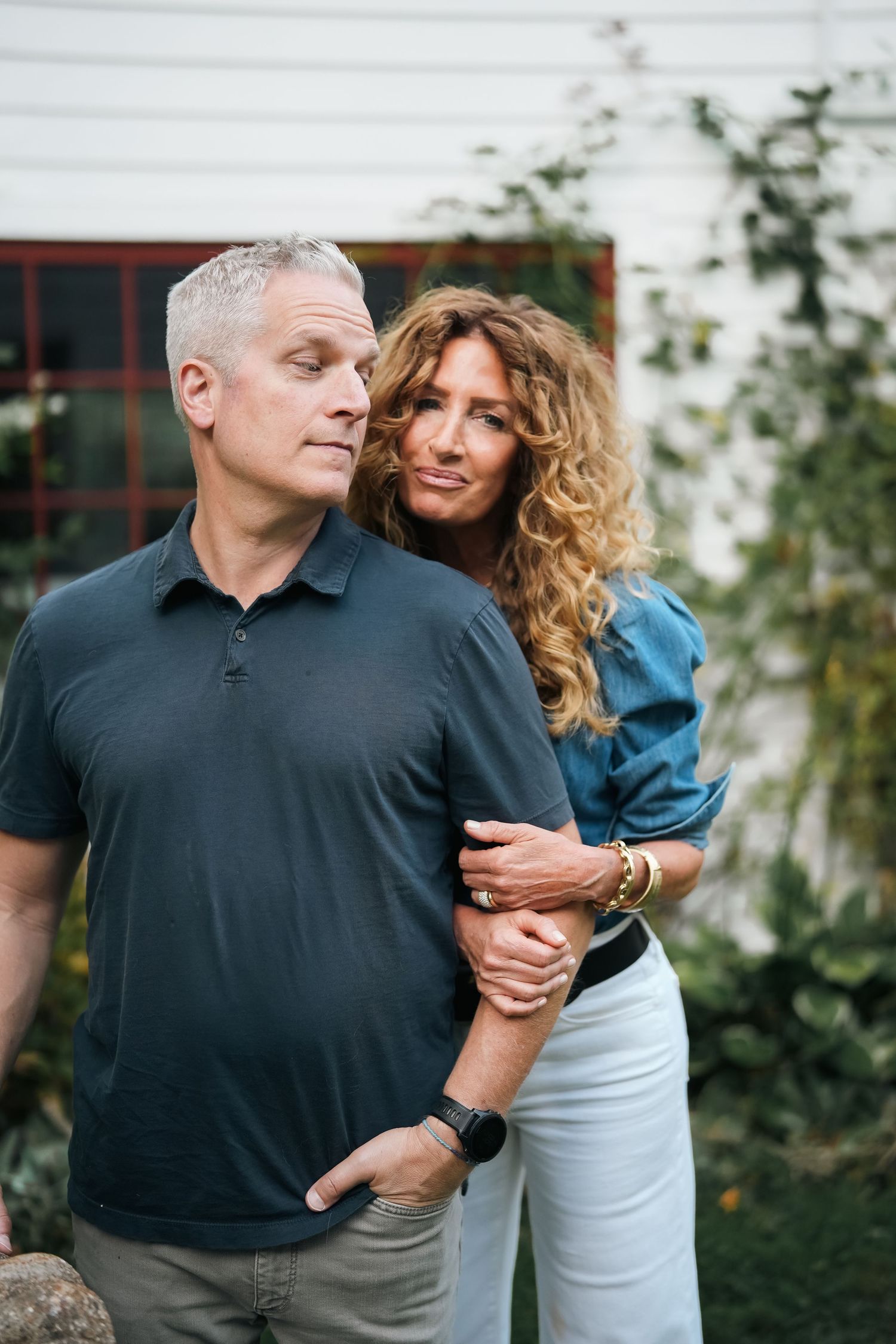 Intimate couple portrait session against white wall with greenery.