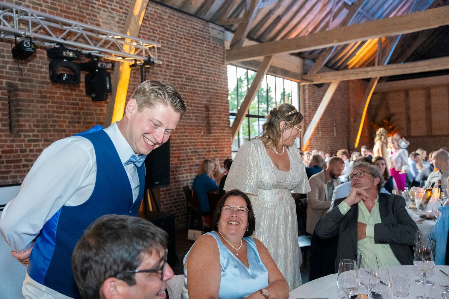 Wedding guests celebrate during a reception in a brick-walled venue with exposed wood beams.