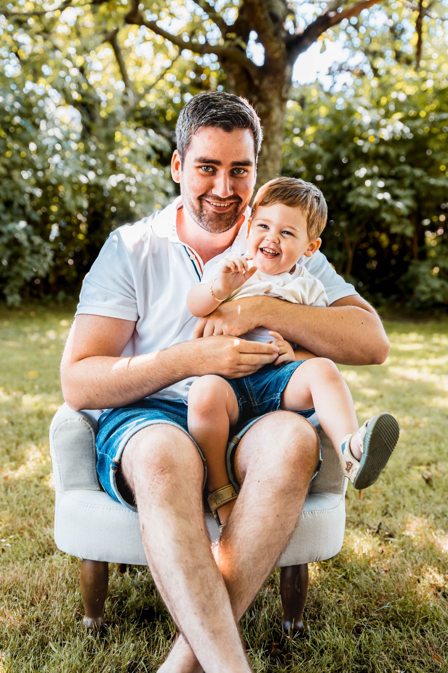 Joyful moment shared between parent and child sitting in white chair on sunny lawn.