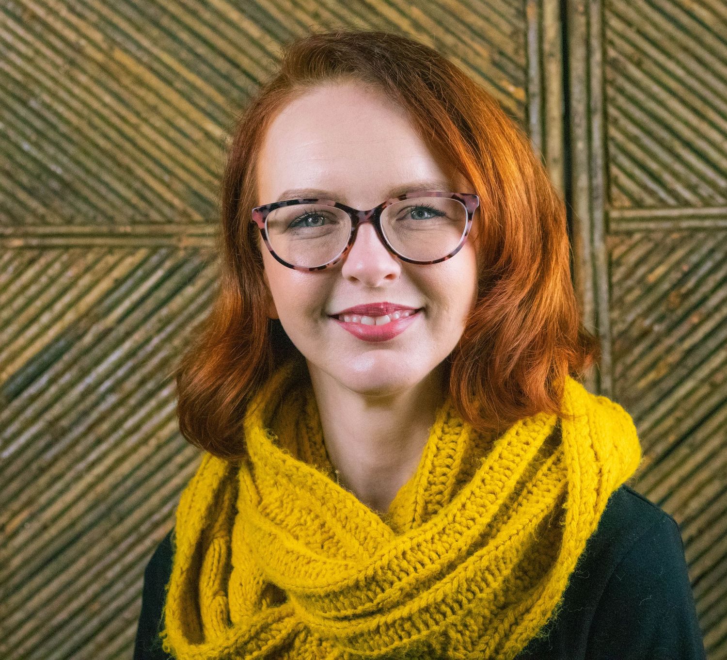 Portrait featuring bright yellow scarf and glasses against geometric patterned wall.