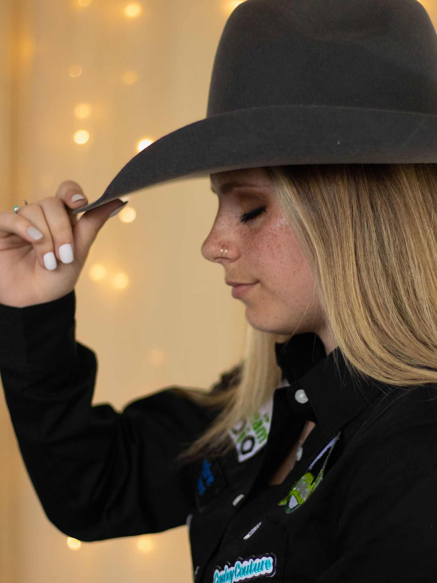Side profile of someone in black hat and jacket with string lights in background.