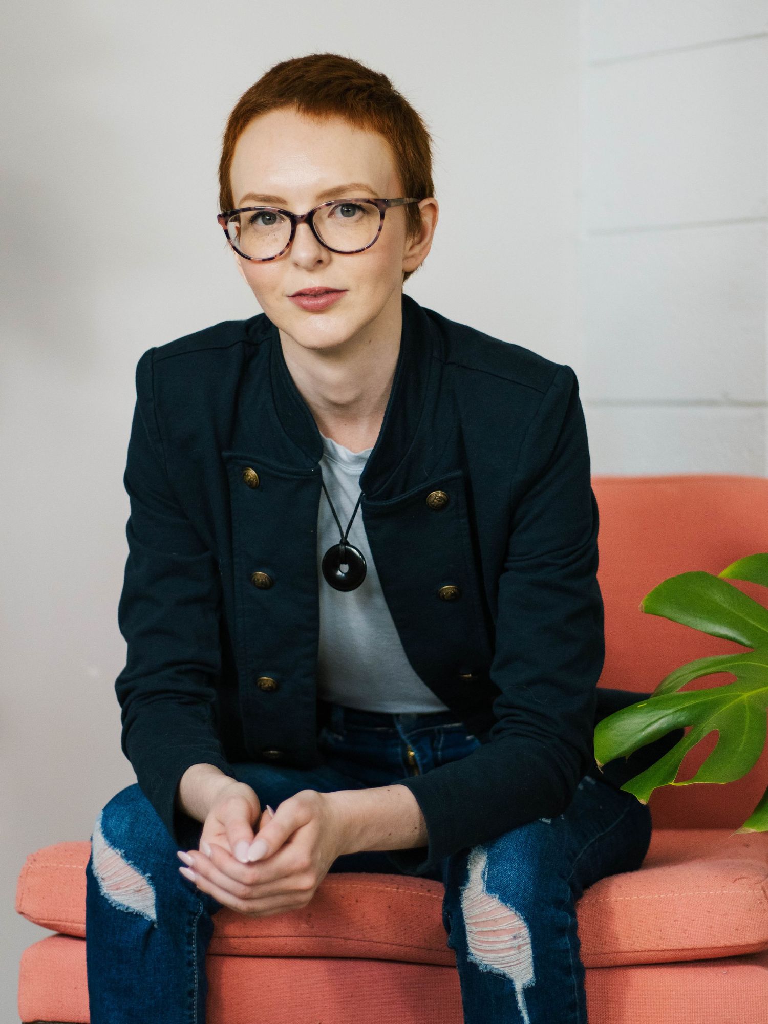 Stylish portrait against white wall showing navy blazer, glasses and casual denim look.