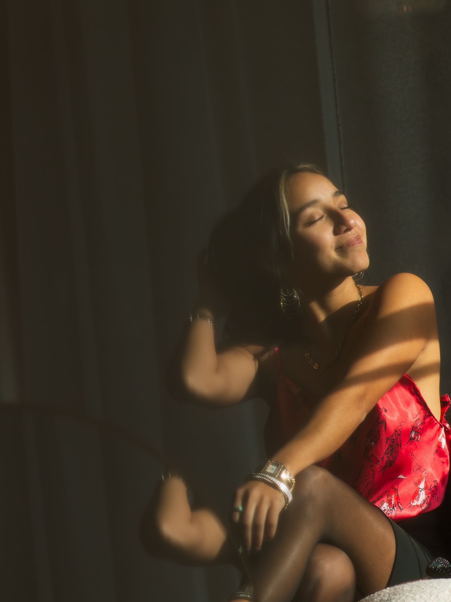 Moody portrait in dramatic lighting shows figure in red wearing bracelet with eyes closed in contemplative pose.