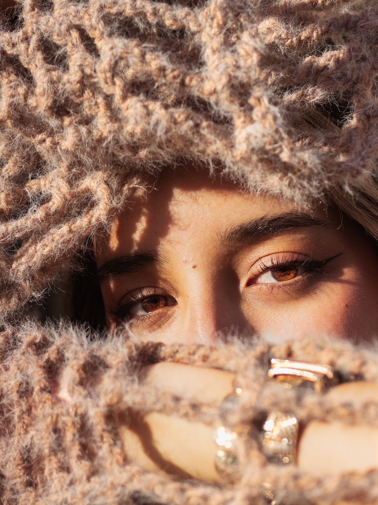 Close-up artistic portrait through textured knit fabric with warm sunlight.