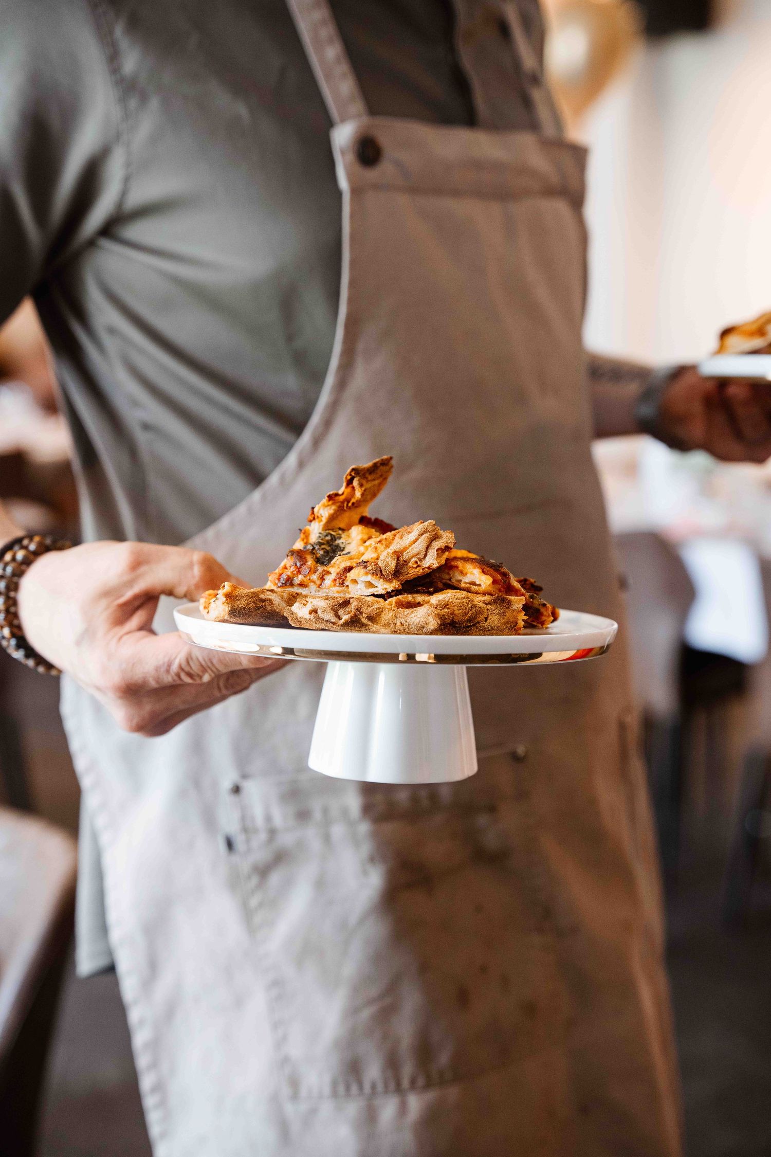 Server in gray apron holding plated crispy chicken dish.