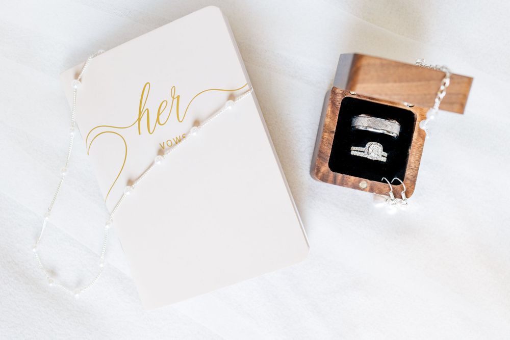 Elegant white wedding vow book with gold lettering next to small black box.