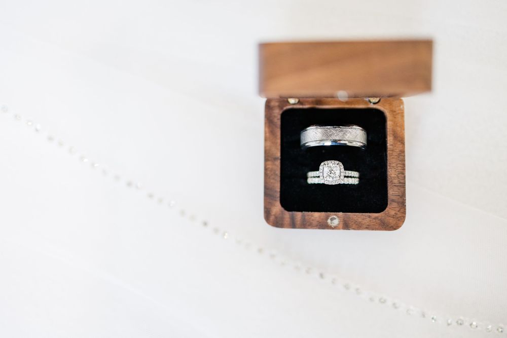 Diamond engagement ring displayed in small wooden ring box with rustic wood texture background.