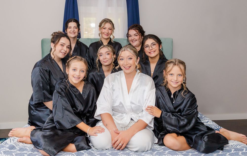 Group photo of bridal party in matching black robes with bride in white center.