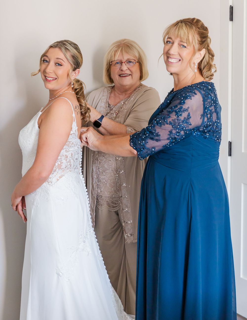 Getting ready scene showing three people helping with wedding dress preparations.