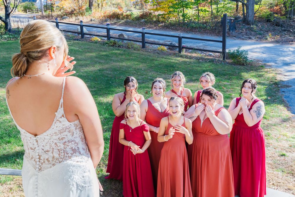 Bridesmaids in red dresses react with surprise and delight as they see the bride in her wedding gown.