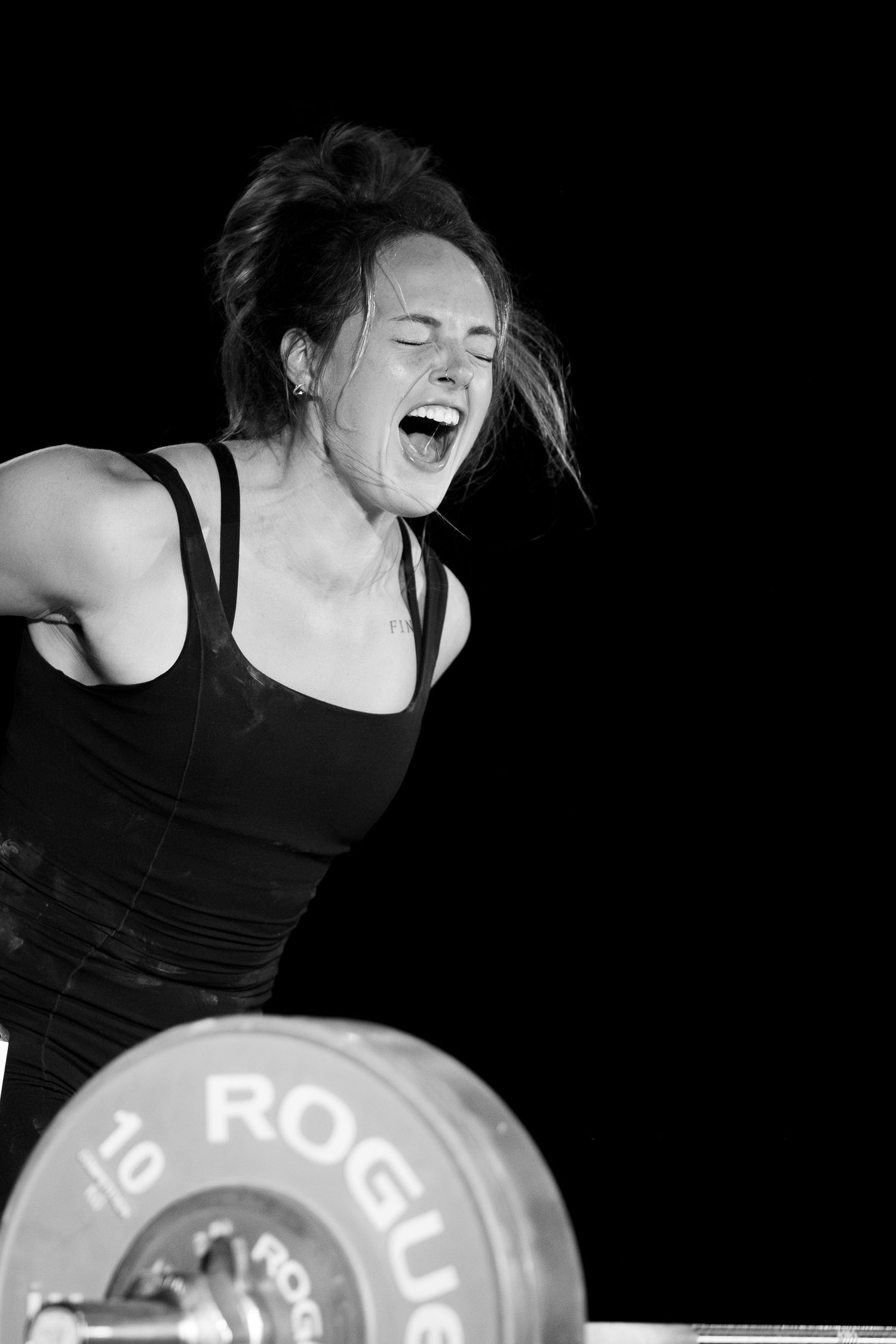 Black and white photo of weightlifter during intense Olympic lift with Rogue barbell.
