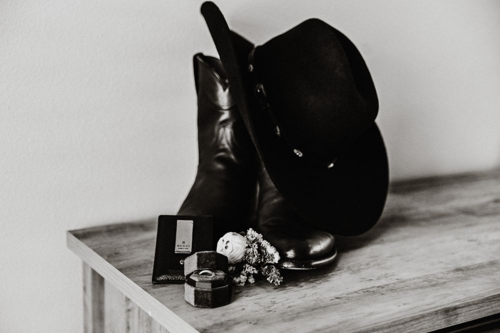 Black cowboy hat and boots arranged with wedding rings in monochrome still life.
