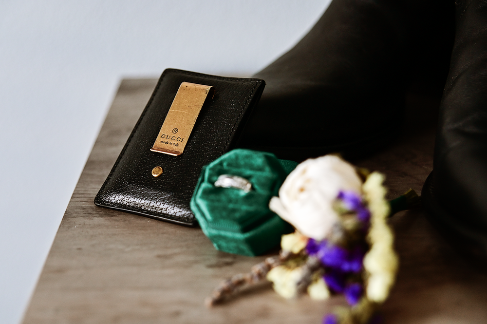 Wedding details featuring green accessories and purple flowers with black perfume bottle.