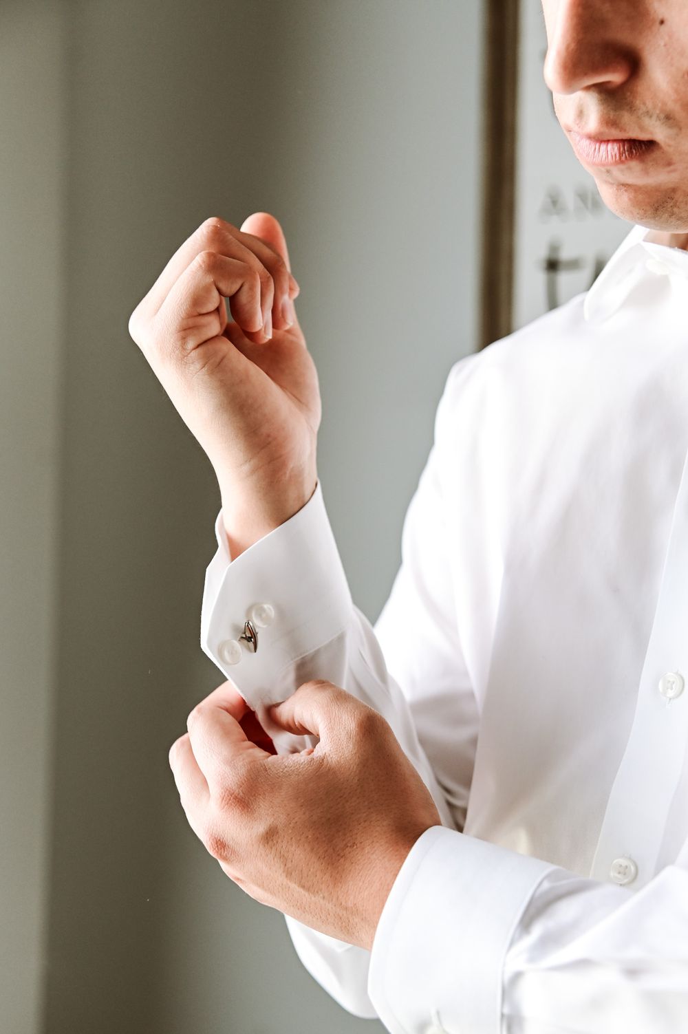 Close-up of hands adjusting white dress shirt cuff links in elegant formal attire.