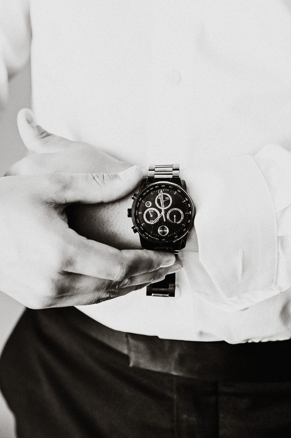 Black and white detail shot of hands adjusting luxury chronograph watch.