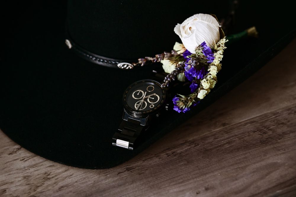 Wedding accessories featuring a black watch with floral boutonniere against dark background.