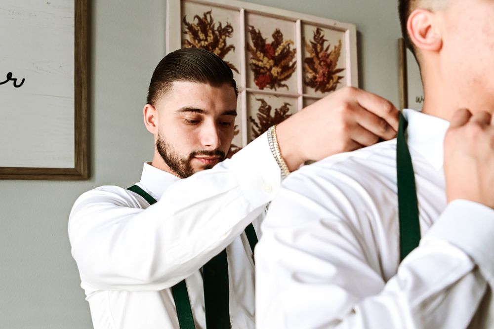Groomsmen helping each other get dressed in formal wedding attire.
