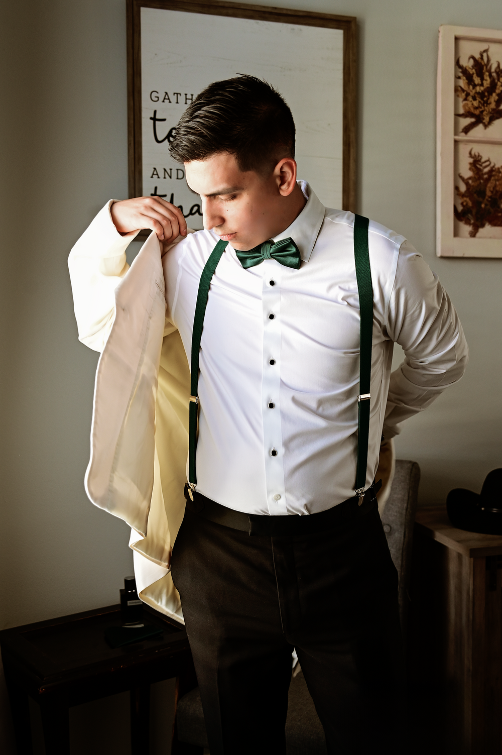 Person in formal attire with green suspenders and bow tie getting dressed.
