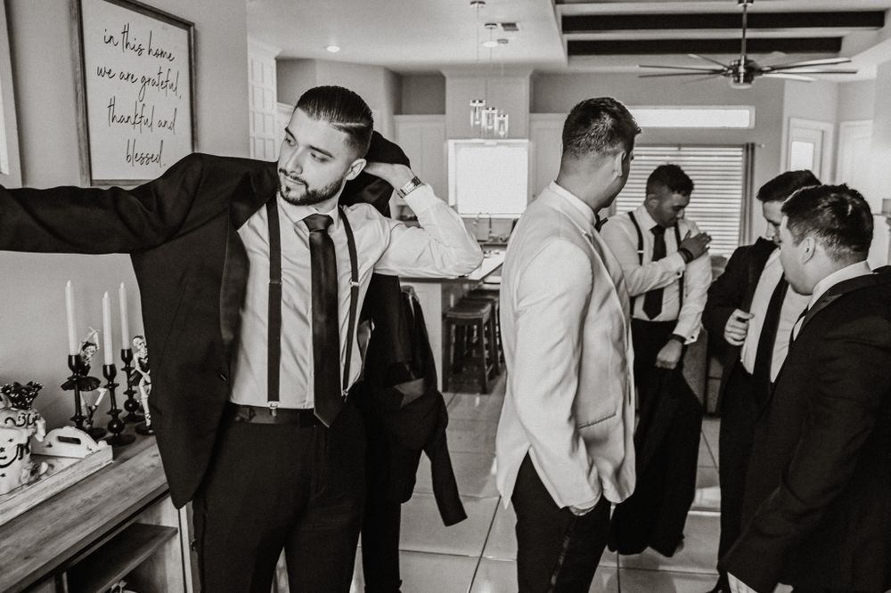 Groomsmen getting ready in a room with exposed wooden beams and white walls.