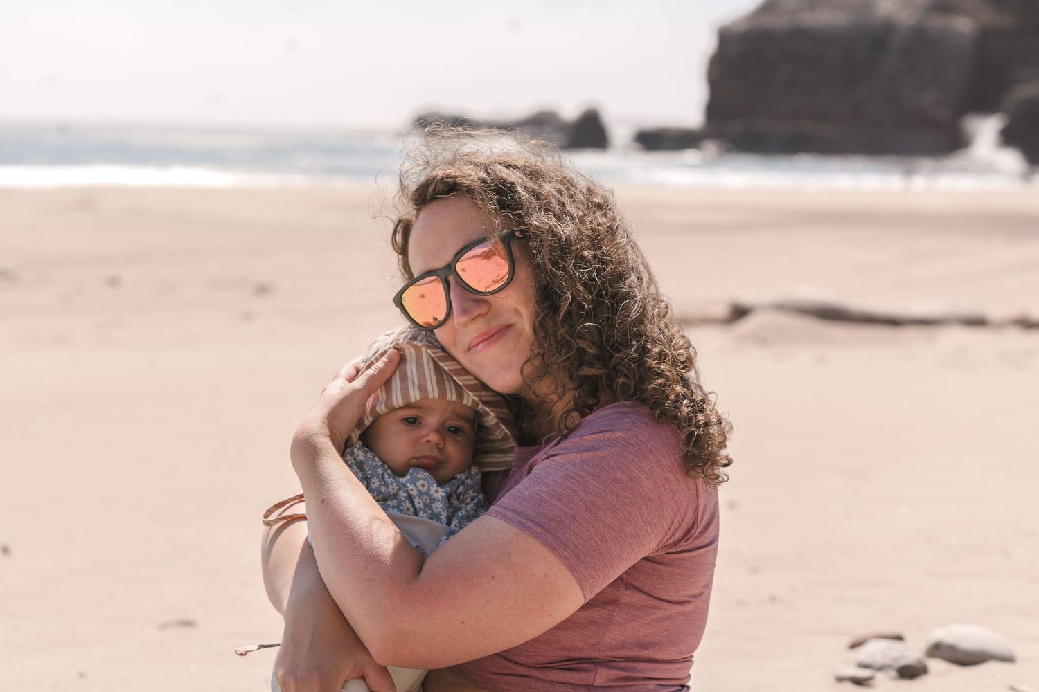 Tender family moment shared on sandy beach with ocean cliffs in background. Located near Santa Cruz, CA.