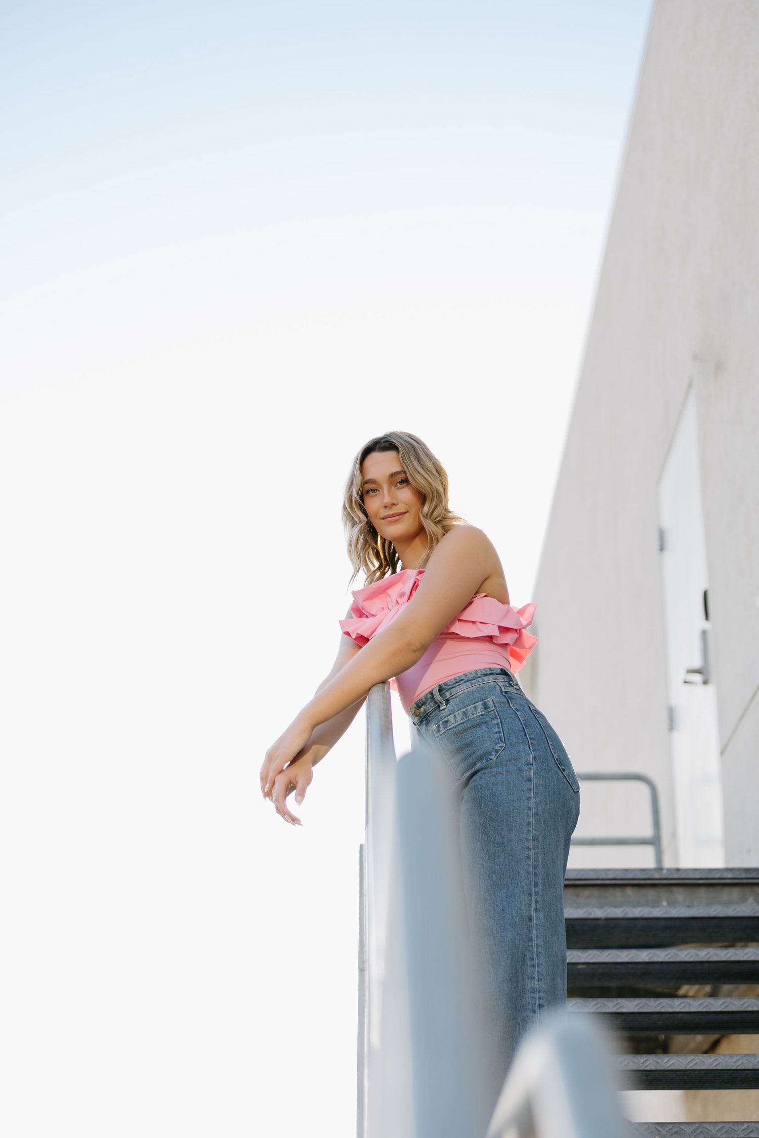 Summer fashion look captured on industrial staircase with pink top and classic denim.