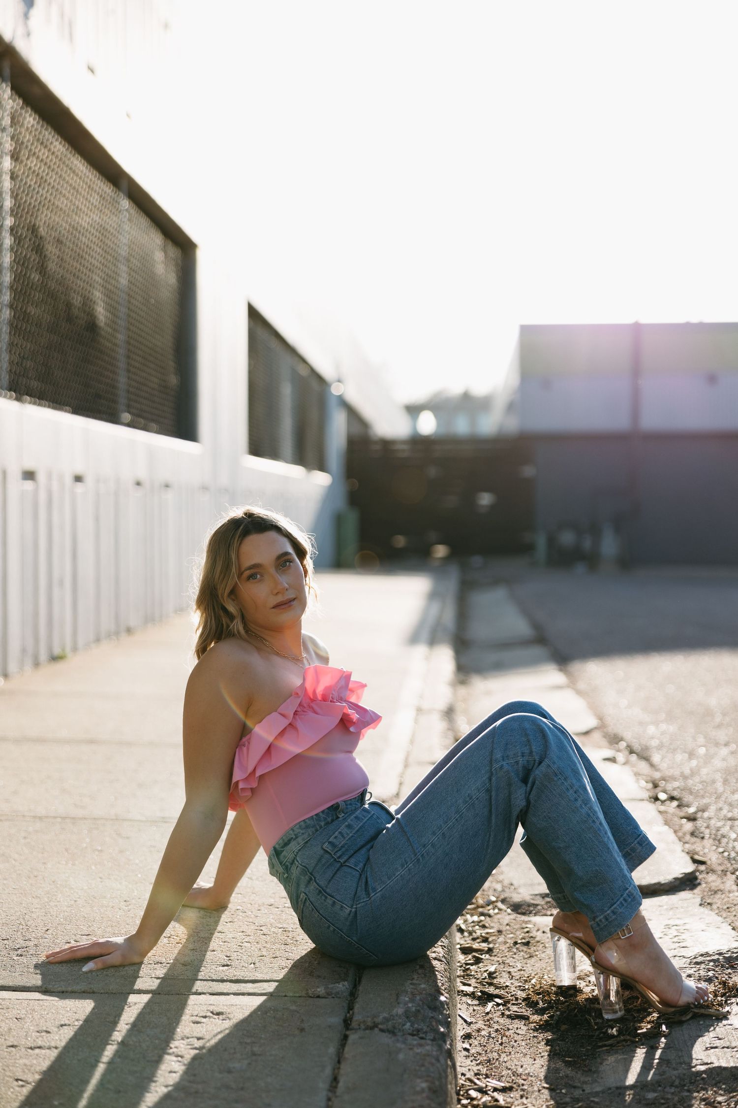 Street style photo with pink ruffle top and relaxed denim in urban setting with sunlight.