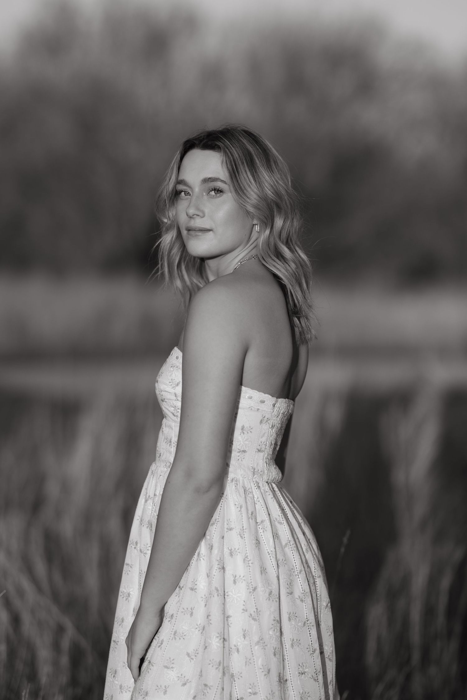Black and white portrait of woman in strapless dress standing in outdoor field setting.