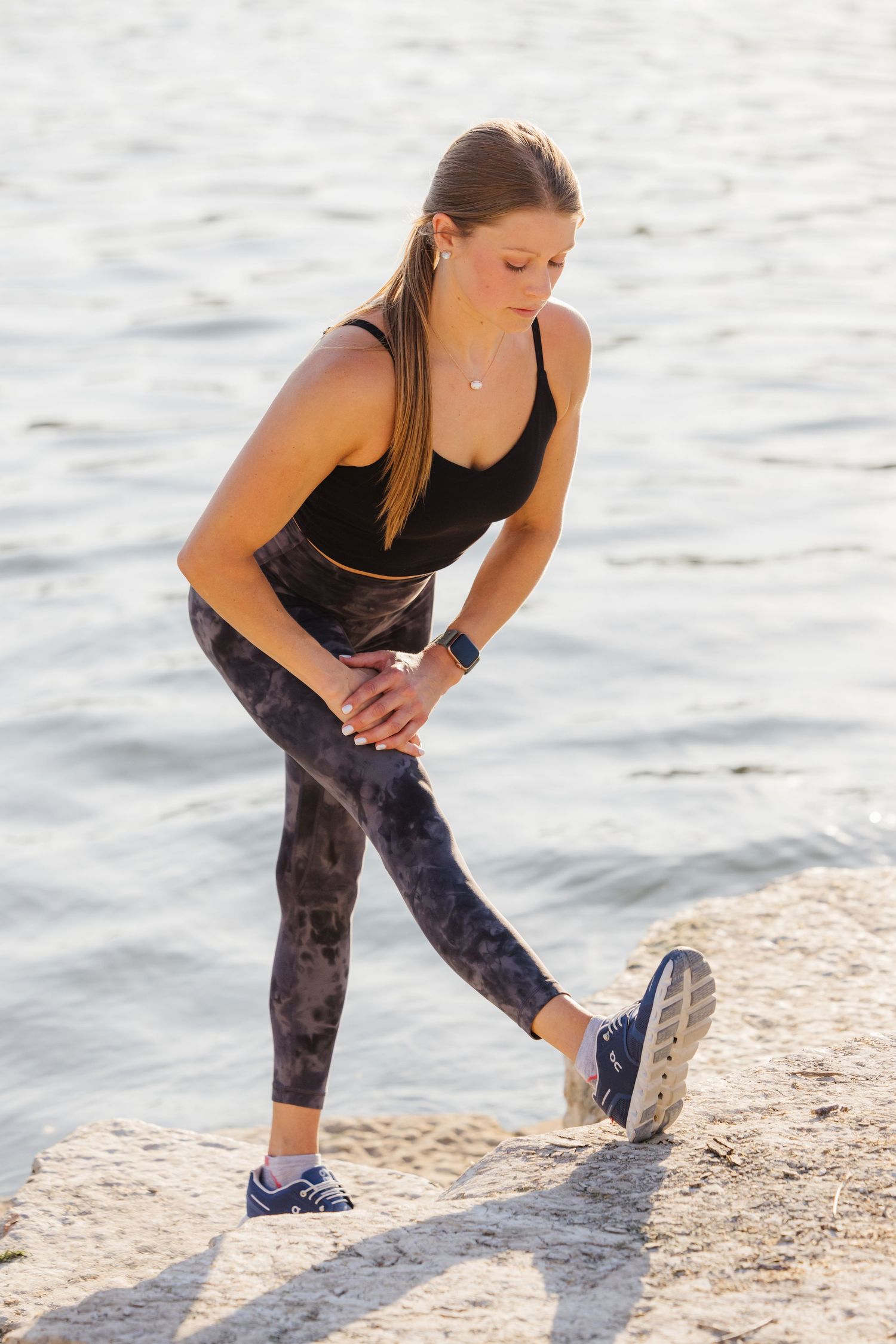 Person in activewear stretches leg muscles on a shoreline during sunset.
