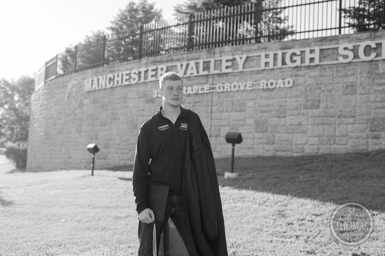 Black and white portrait of graduate standing by school entrance wall.