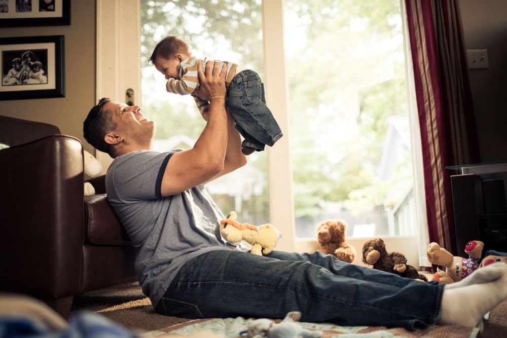 A joyful moment between parent and child playing together on a couch in sunlit living room.