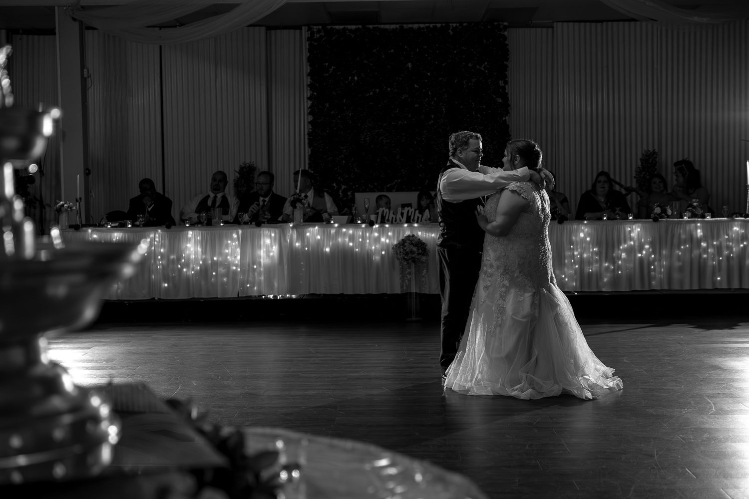 A couple shares their first dance at a wedding reception with string lights glowing in the background.