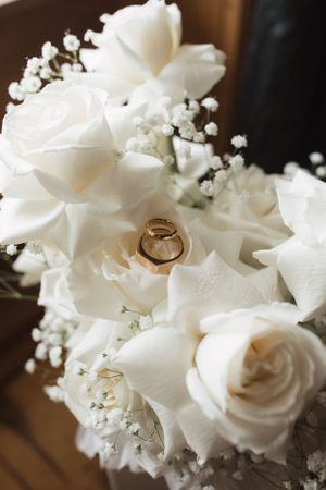 Wedding rings nestled among white roses and delicate baby's breath flowers in bridal bouquet.