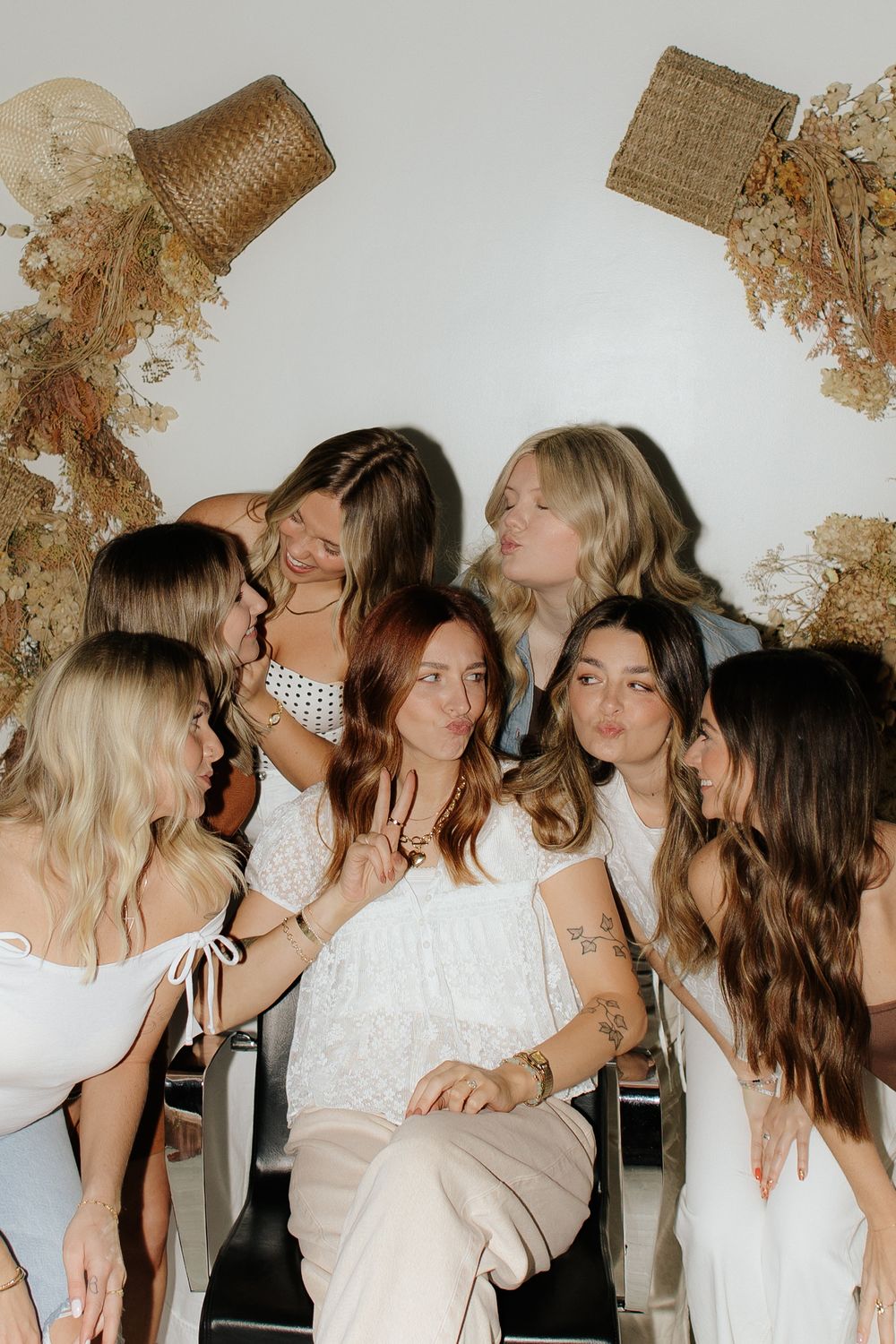 Group wearing white outfits gathered closely together at an indoor event with dried floral decor.