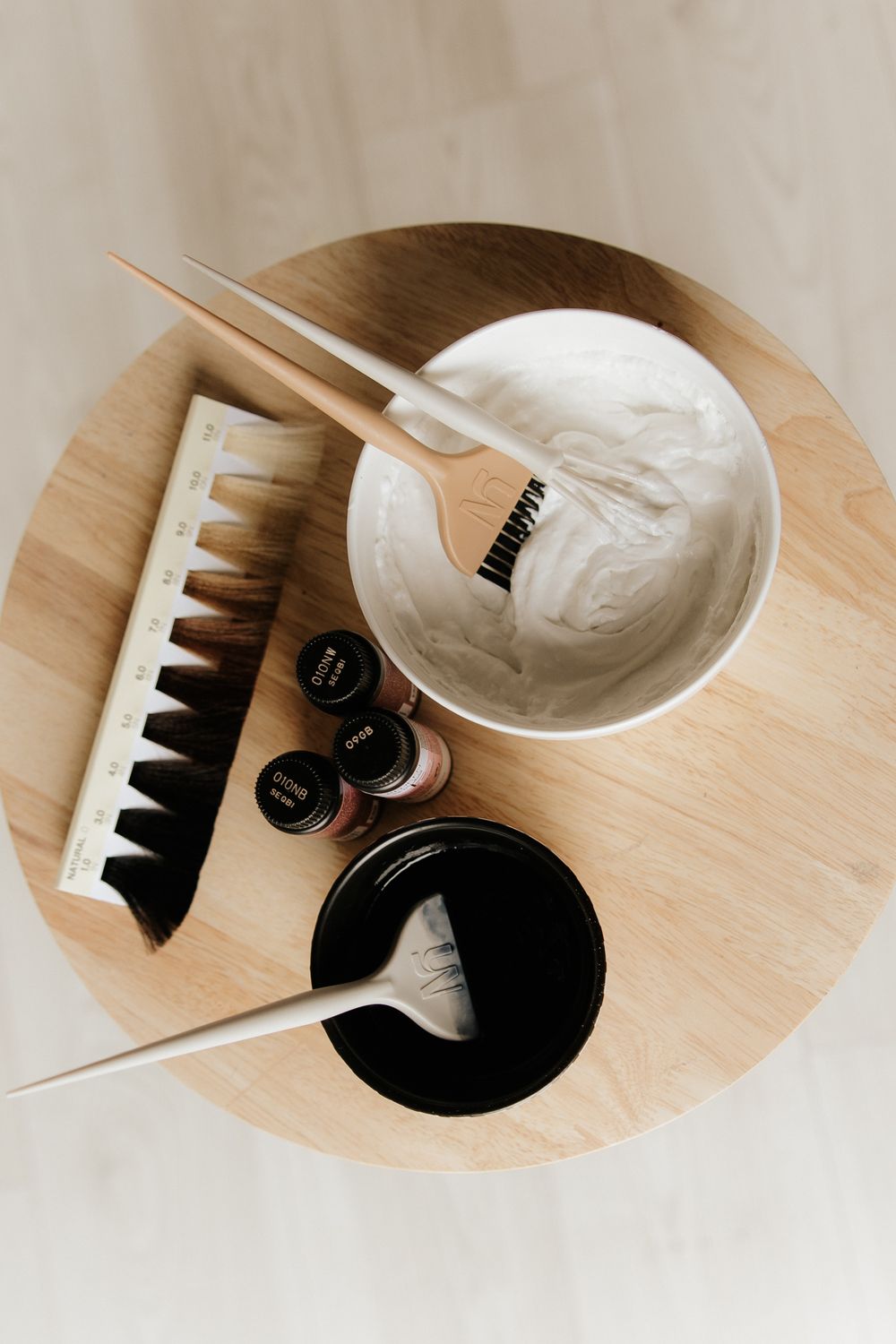Hair dye mixing tools on wooden surface including bowl, brush and product bottles arranged in minimalist style.